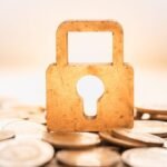 a wooden security lock sits on top of coins to represent a secured loan