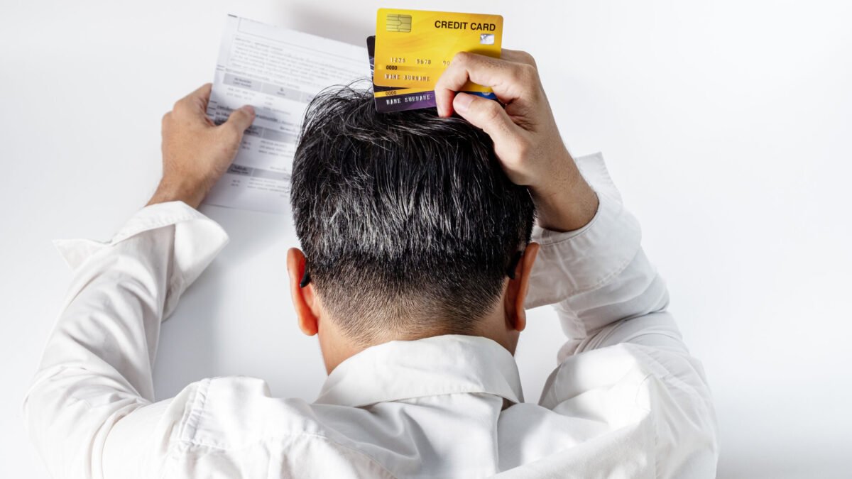 Stressed man holding credit cards grabs head in frustration while looking at credit score