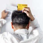 Stressed man holding credit cards grabs head in frustration while looking at credit score