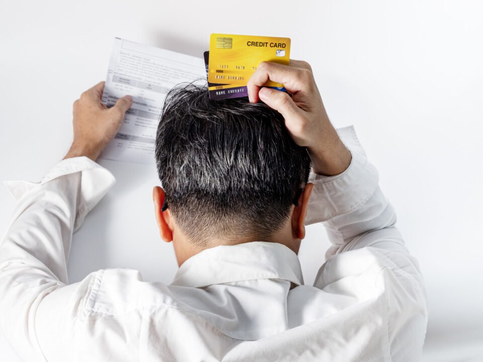 Stressed man holding credit cards grabs head in frustration while looking at credit score